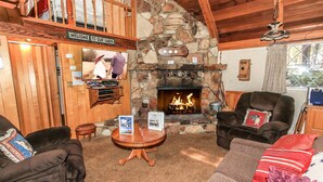 Interior acogedor de una cabaña con chimenea de piedra, muebles de madera y un letrero de bienvenida.