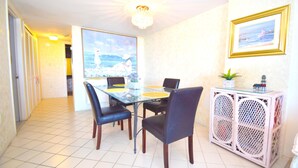 Un coin repas comprenant une table en verre, des chaises noires, un meuble blanc avec un plateau en verre et un tableau accroché au mur.