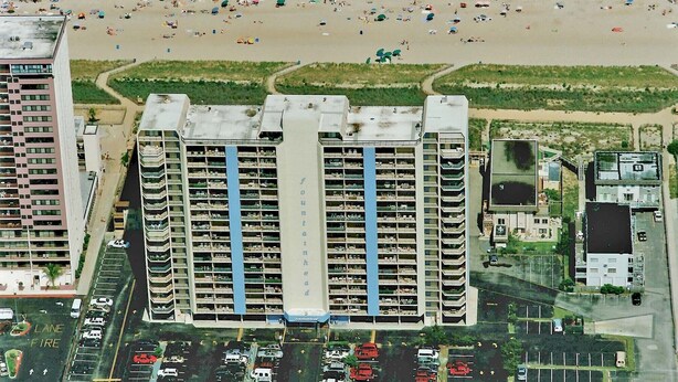 Un immeuble de grande hauteur, avec de nombreux étages, un parking et une plage en arrière-plan.