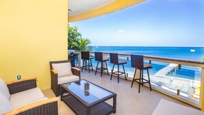 A balcony with wicker furniture, a glass coffee table, and a view of the ocean. - Best location in West End -Pool, Kayaks, & Large Balcony (Roatan)