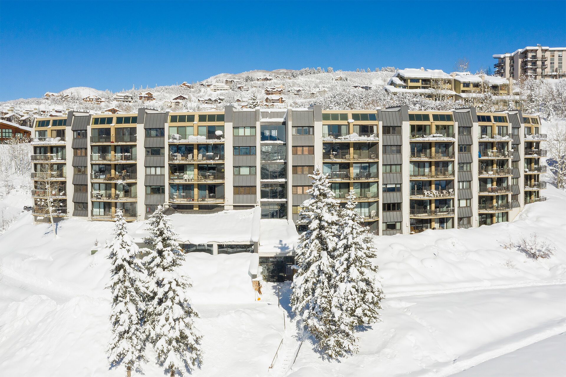 A multi-story hotel with balconies, surrounded by snow-covered trees and buildings.