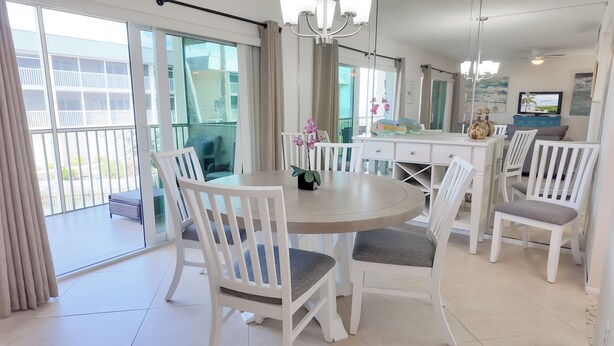 A dining area with a round table and white chairs, a potted orchid, and a view of a balcony with a railing. - Serene and Relaxing (Sanibel)