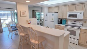A modern kitchen with a central island, two bar stools, a refrigerator, a microwave, and an oven. - Serene and Relaxing (Sanibel)