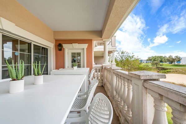 A balcony with a white table and chairs, potted plants, and a view of a golf course. - Sunset View | Stunning Golf Views Close to Disney! Luxury Condo Near Disney! (Kissimmee)