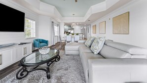 A modern living room with a glass coffee table, a white sofa, and a ceiling fan. - Sunset View | Stunning Golf Views Close to Disney! Luxury Condo Near Disney! (Kissimmee)