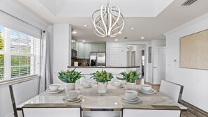A modern dining area with a central table set for four, surrounded by white chairs. - Sunset View | Stunning Golf Views Close to Disney! Luxury Condo Near Disney! (Kissimmee)