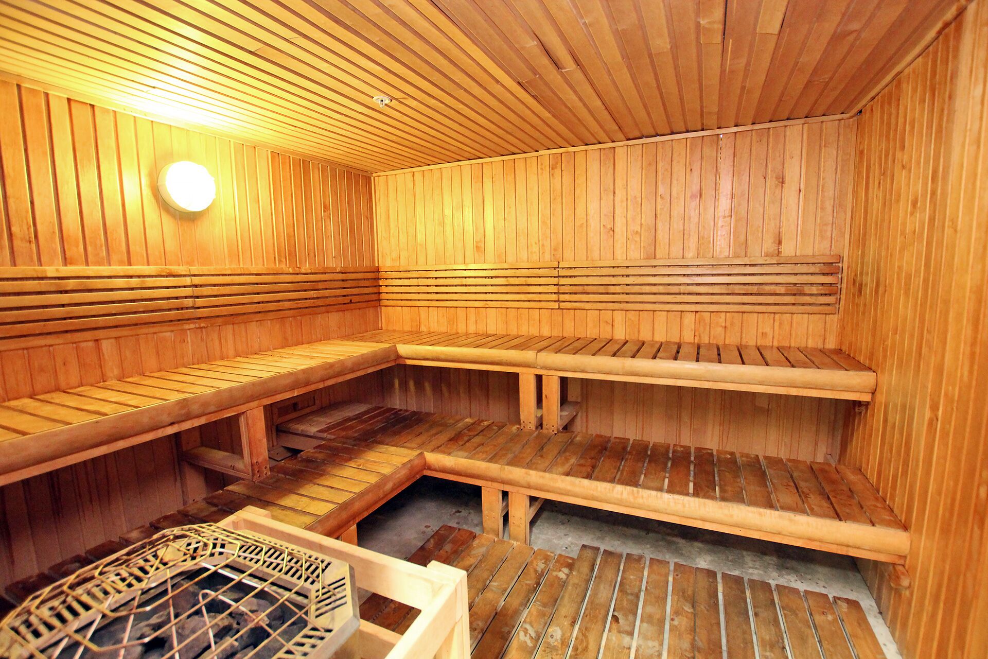 Una sauna de madera con bancos y una estante con rejilla de metal.