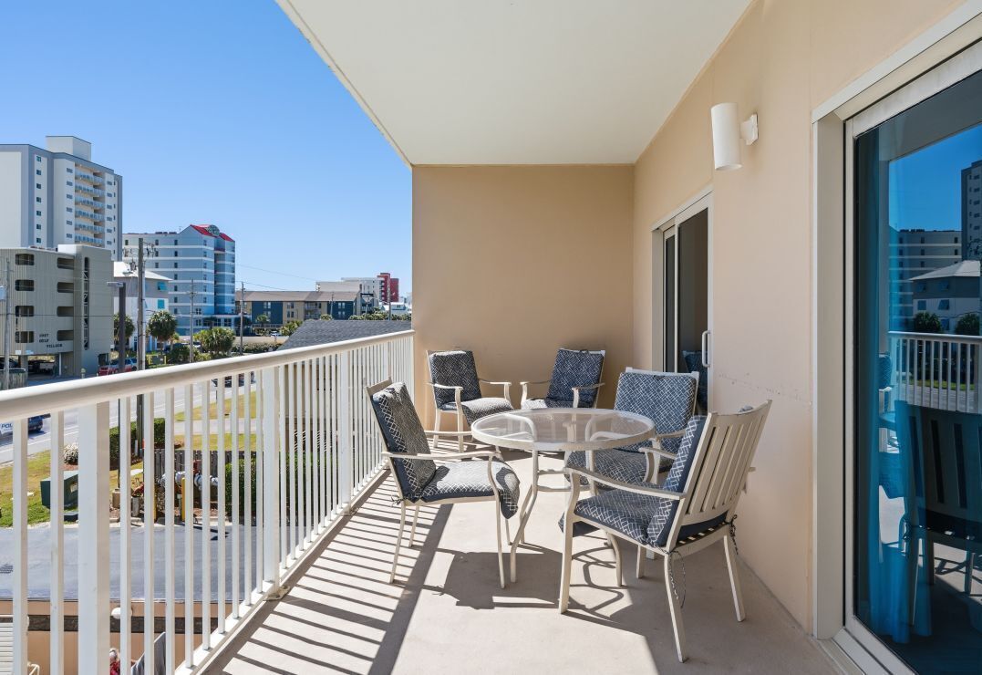 Un balcon avec une table ronde et des chaises, une balustrade blanche et une vue sur les bâtiments en arrière-plan.