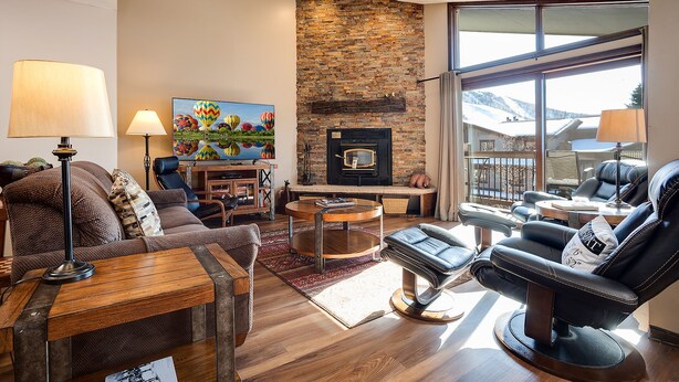 A modern living room with a stone fireplace, comfortable seating, and a large window offering a view of the outdoors.