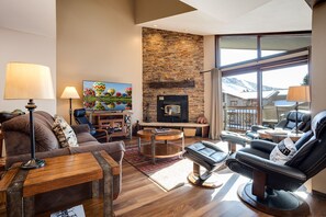Una sala de estar moderna con chimenea de piedra, asientos cómodos y un gran ventanal con vistas al exterior.