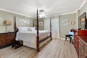 A four-poster bed with a canopy, a wooden dresser, a vanity with a mirror, and a small table with a lamp.