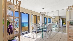 A spacious balcony with a glass table and chairs, a wicker chair, and a shelf with decorative items.