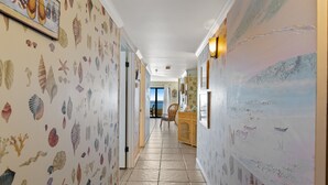 A hallway with a sea shell wallpaper, a wooden cabinet, and a view of the ocean through a window.