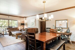 A spacious living room with a wooden dining table, leather sofas, and a chandelier.