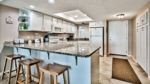 A modern kitchen with white cabinets, a granite countertop, and a built-in island with bar stools. - El Matador 413 by Alicia Hollis Rentals FREE TICKETS! $300/Day (Fort Walton Beach)