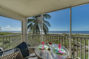 Ein Balkon mit Glastisch, zwei Stühlen und Blick auf Strand und Meer.
