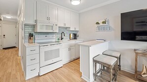 A modern kitchen with white cabinetry, a central island, and a small bar area. - Oceanside Oasis - Breathtaking Views and Coastal Comfort! (Hilton Head)