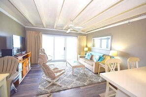Ein Wohnzimmer mit einer Couch, Sesseln, einem Couchtisch, einem Fernseher und einem Deckenventilator.