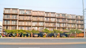 A multi-story residential building with balconies, a parking area, and a clear sky. - Jada 4H-Oceanside 77th St, Free WiFi, Pool, Elev, W/D, AC (Ocean City)