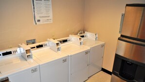 Un área de lavandería con cuatro lavadoras blancas, un refrigerador de acero inoxidable y un dispensador de agua.