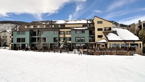 Un hotel de varios pisos con tejado nevado, un telesilla y montañas al fondo.
