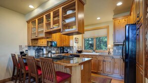 A kitchen with wooden cabinets, a central island with bar stools, a refrigerator, and a window with blinds.