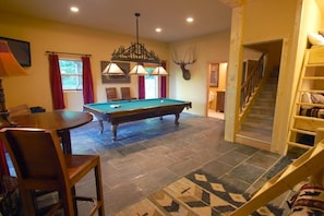 A pool table in a room with a staircase and a wooden ladder.