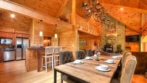 Interior de una cabaña de madera con comedor, cocina y una chimenea de piedra.