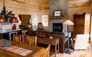Interior acogedor de una cabaña con chimenea de piedra, muebles de madera y un comedor.