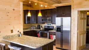 A kitchen with wooden walls, dark cabinets, stainless steel appliances, and a granite countertop. - Stargazer - Free Train Tix + Modern-Rustic Cabin (Bryson City)