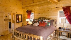 A wooden cabin bedroom with a rustic bed, a nightstand, and a window with curtains. - Stargazer - Free Train Tix + Modern-Rustic Cabin (Bryson City)