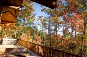 Una terraza de madera con jacuzzi y zona de estar con vista a un bosque con follaje otoñal.
