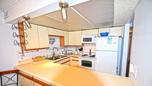 A compact kitchen with a central island, white appliances, and a hanging light fixture. - Thunder Island 10A-Baywater 39th St, Pool, Elev, W/D, AC (Ocean City)