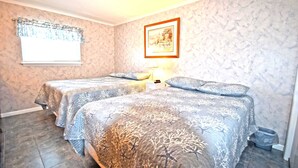 A room with two beds, a window with a curtain, a framed picture on the wall, and a small table with a lamp. - Thunder Island 10A-Baywater 39th St, Pool, Elev, W/D, AC (Ocean City)
