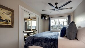 Ein Schlafzimmer mit Bett, Deckenventilator, Fenster mit Vorhängen und einem Essbereich mit Tisch und Stühlen.