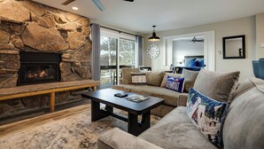 Ein gemütliches Wohnzimmer mit Kamin aus Stein, Deckenventilator und großem Fenster.