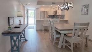 Una cocina moderna con armarios blancos, un refrigerador de acero inoxidable y un comedor con sillas blancas y una mesa de madera.