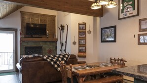 A cozy living room with a fireplace, wooden furniture, and a television mounted on the wall. - Condo with Excellent Mountain Views (Whitefish)