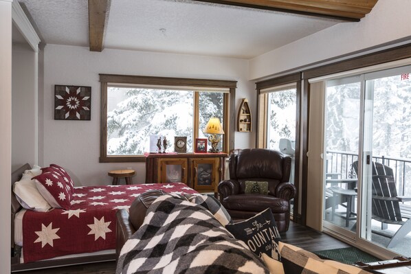 Um quarto aconchegante com uma cama, uma poltrona de couro, um armário de madeira e uma grande janela com vista para árvores cobertas de neve.