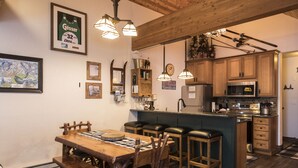 A kitchen with wooden cabinets, a central island with stools, a microwave, and a hanging light fixture. - Condo with Excellent Mountain Views (Whitefish)