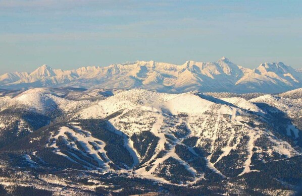 A mountainous landscape with snow-covered peaks and dense forests. - Condo with Excellent Mountain Views (Whitefish)