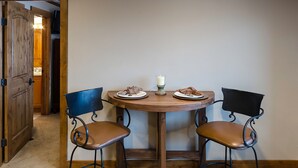 Un comedor con una mesa redonda de madera, dos sillas con estructura metálica y un centro de mesa con una vela.