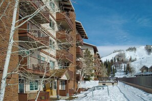 A multi-story building with balconies, a ski slope in the background, and a clear sky.