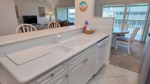 Een moderne keuken met witte kasten, een dubbele spoelbak en een eetgedeelte met een tafel en stoelen.