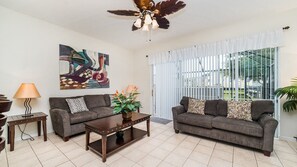 Relax in this stylish living room with two sofas, a coffee table, and a floor lamp, surrounded by a large abstract painting and large windows with a view.