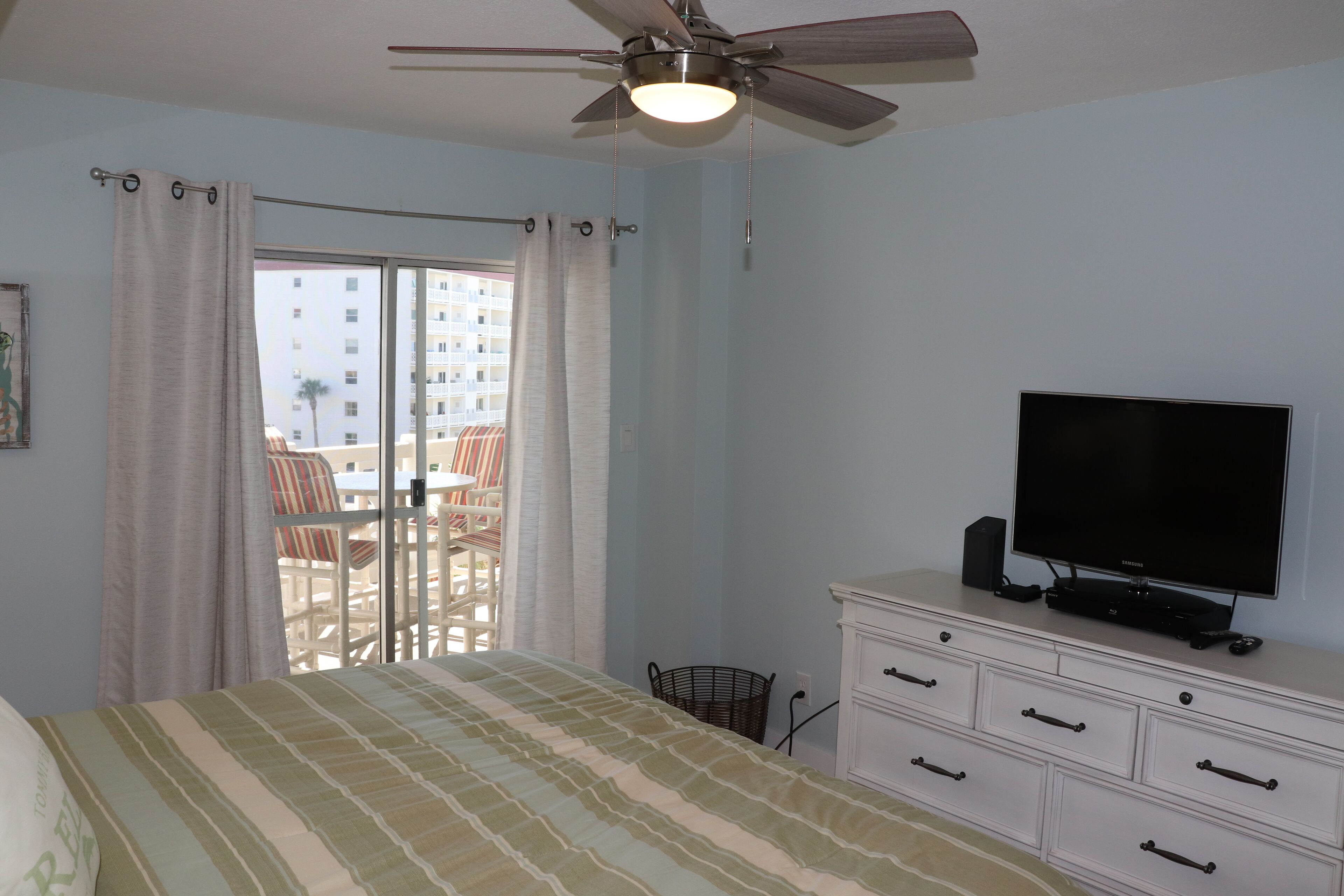 A bedroom with a bed, a television on a dresser, and a balcony with chairs.