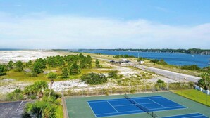 A tennis court with a clear view of the surrounding landscape, including a body of water and distant buildings.