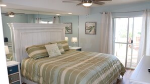 A bedroom with a large bed, a nightstand, a dresser, a ceiling fan, and a sliding glass door leading to an outdoor area.
