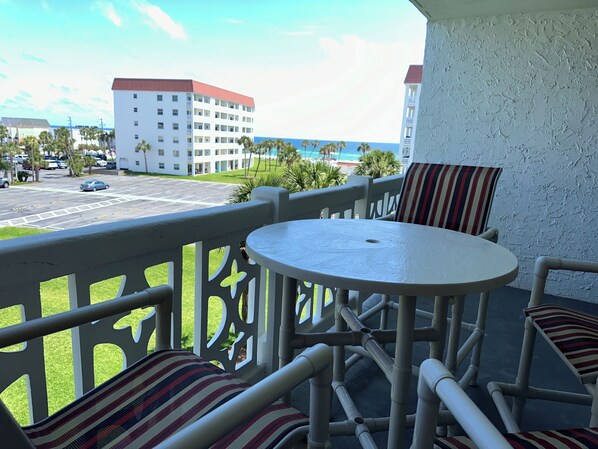 Een balkon met een tafel en stoelen, met uitzicht op een parkeerplaats en gebouwen.
