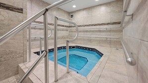 A pool area with a glass-enclosed hot tub, metal railings, and tiled walls.